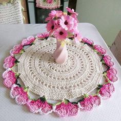 a crocheted doily with pink flowers in a vase sitting on a table