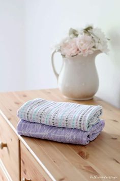 two folded towels sitting on top of a wooden table next to a vase with flowers