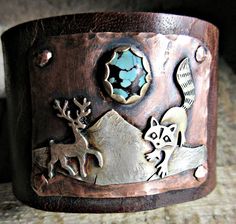 Into the Wild Distressed Wide Leather Cuff bracelet by Weathered Soul Jewelry, raccoon, artisan made, rustic, Buck, Deer, Antlers, OOAK, USA This is truly and amazing piece. It is wide Buffalo hide distressed leather with 2 heavy duty bronze snaps set for a 7 inch wrist size. Keep in mind they fit a little snugger than usual with wide leather so this could fit a tad smaller wrist still. Genuine turquoise matrix stone set in silver on copper. Raccoon and Deer are sterling as well as the mountains Rustic Handmade Cuff Bangle Bracelet, Handmade Rustic Style Bangle Jewelry, Handmade Rustic Bangle Jewelry, Rustic Handmade Bangle Jewelry, Rustic Adjustable Stamped Cuff Bracelet, Rustic Stamped Adjustable Cuff Bracelet, Rustic Stamped Cuff Bracelet Gift, Handmade Artisan Cuff Bracelet, Artisan Cuff Bracelet With Unique Variations