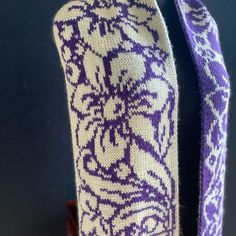 a purple and white knitted neck tie sitting on top of a wooden table next to a blue wall