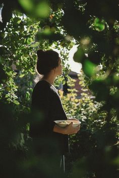 a woman holding a plate in her hands while standing next to some bushes and trees