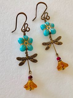 "Adorable turquoise blue Czech glass puffed daisies with topaz yellow bellflowers and vintage bronze stamped dragonfly charms. Matte turquoise 14 mm Czech glass puffy 5 petal flowers are etched with metallic gold and wire wrapped in vintage bronze with 6 x 9 mm translucent topaz yellow bellflowers accented with tiny burnt orange crystals. Lightweight dangles hang on handmade and hammered vintage bronze ear wires. Total drop length is 2 1/2\"." Whimsical Blue Jewelry With Flower Charm, Blue Bohemian Flower Earrings, Whimsical Adjustable Nickel-free Flower Earrings, Whimsical Blue Nickel-free Earrings, Vintage Turquoise Dangle Flower Earrings, Whimsical Handmade Turquoise Earrings, Vintage Turquoise Flower Earrings, Handmade Blue Whimsical Flower Earrings, Whimsical Handmade Blue Flower Earrings