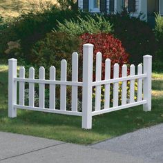 a white picket fence in front of a house with red bushes and shrubs around it