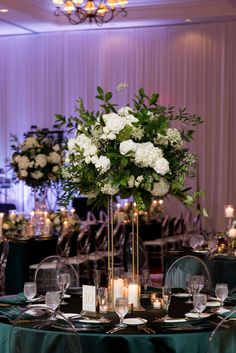 a tall vase with white flowers and greenery sits on top of a round table