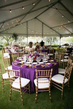 tables set up under a tent with purple linens and white chairs for an event