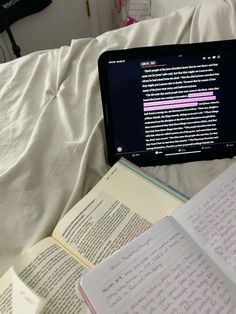 an open laptop computer sitting on top of a bed next to notebooks and books