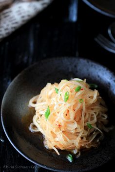 a black plate topped with noodles and scallions