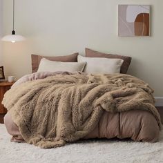 a bed with a fluffy blanket on top of it next to a night stand and lamp