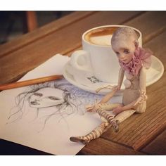 a doll sitting on top of a table next to a cup of coffee and pencil