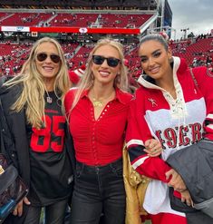 three beautiful women standing next to each other at a football game