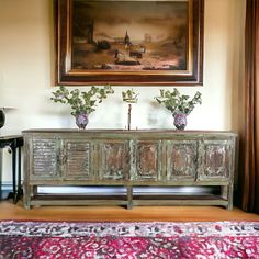 two vases with flowers sit on top of an old wooden sideboard in front of a painting