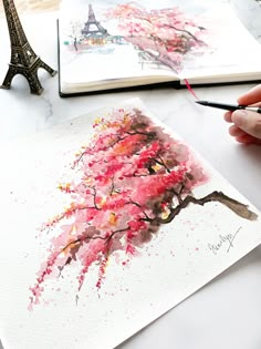 a person is drawing with watercolors in front of the eiffel tower