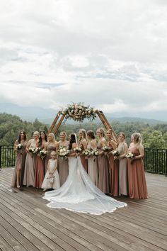 a group of women standing next to each other in front of a wedding arch on top of a wooden deck