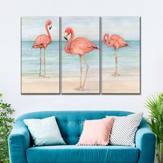 three pink flamingos standing on the beach in front of blue couch and wall art