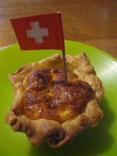 a pie with a swiss flag sticking out of it on a green plate next to a wooden table