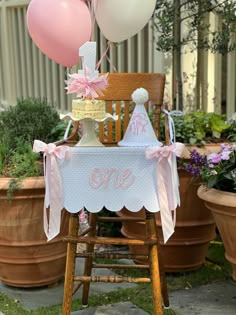 a baby's first birthday party with balloons and cake on a chair in front of potted plants