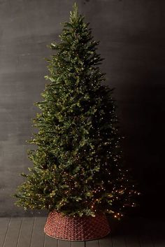 a small christmas tree in a red basket on a wooden floor next to a wall