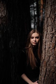 a woman standing next to a tree in the woods