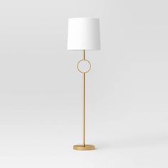 a gold floor lamp with a white shade on the base and a round light fixture