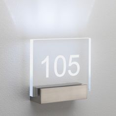 a glass plaque with the number 105 on it is mounted to a wall in front of a white background