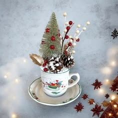 a cup filled with pine cones and other decorations on top of a saucer next to christmas lights