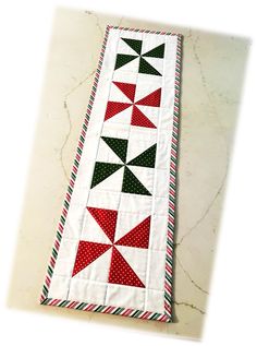 a quilted table runner with red, green and white triangles on the border is sitting on a marble surface