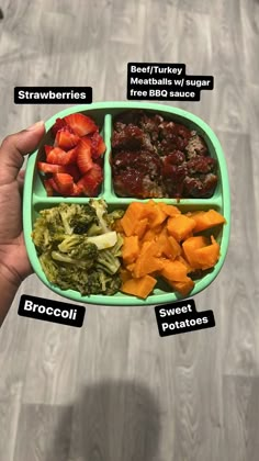 a person holding a green tray with different foods in it that include broccoli, strawberries, and meat