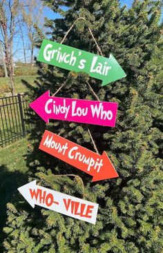 three directional signs hanging from a tree in front of a fence with grass and trees