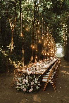 a long table set up with flowers and candles for an outdoor dinner in the woods