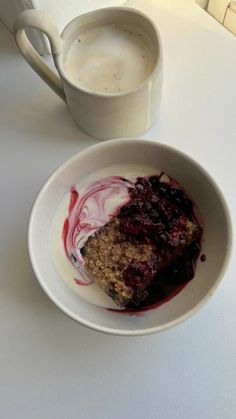 a white bowl filled with food next to a cup of coffee on top of a table