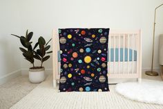 a baby crib with a space themed blanket next to a potted plant on the floor