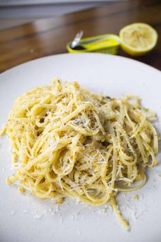 a white plate topped with pasta covered in parmesan cheese next to lemon wedges