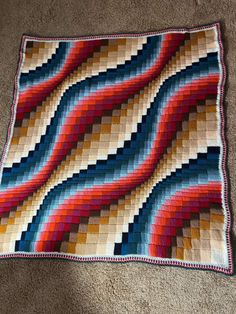 a multicolored crocheted blanket on the floor next to a brown carpet