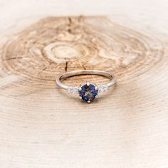 a blue and white diamond ring sitting on top of a piece of wood