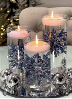 three lit candles sitting on top of a glass tray next to christmas balls and ornaments