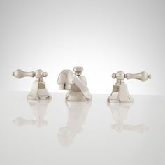 three faucets on a white counter top with reflections in the water below them