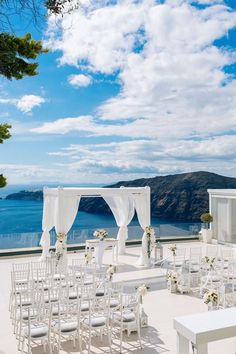 an outdoor wedding setup with white chairs and drapes on the roof overlooking the ocean