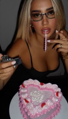 a woman holding a cell phone in front of a heart shaped cake with the word love spelled on it