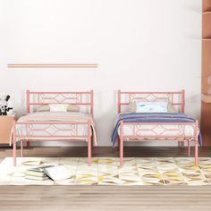 two beds in a room with white walls and wooden flooring, one has pink metal frames