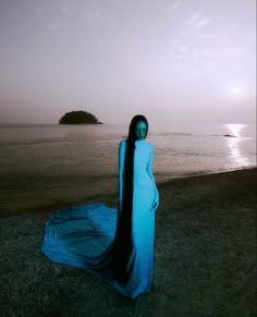 a woman standing on top of a sandy beach next to the ocean wearing a blue dress