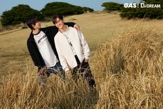 two young men standing next to each other in a field full of tall dry grass