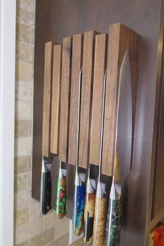 a wall mounted knife holder with six knives hanging from it's sides, and several other kitchen utensils attached to the wall