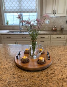 a vase filled with flowers sitting on top of a wooden tray next to candles in front of a window