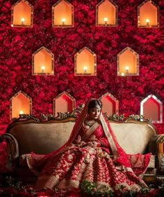 a woman sitting on top of a couch in front of a red wall with candles