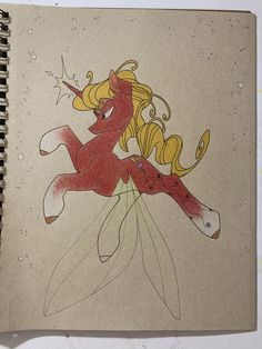 a drawing of a unicorn with blonde hair and stars on it's head, sitting next to a spiral notebook