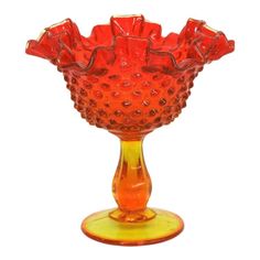 an orange glass vase sitting on top of a yellow stand with red flowers in it