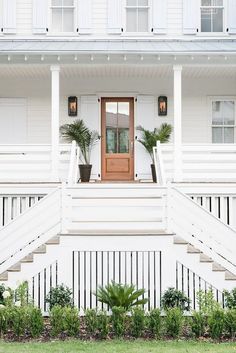 a white house with plants and potted plants on the front steps, along with a wooden door