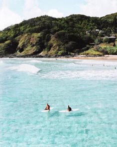 two people on surfboards in the water near a beach with hills and houses behind them