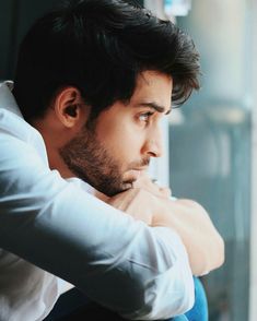 a man leaning against a window with his arm on his chest looking out the window