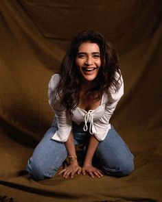 a smiling woman sitting on the ground with her hands in her pockets and legs crossed